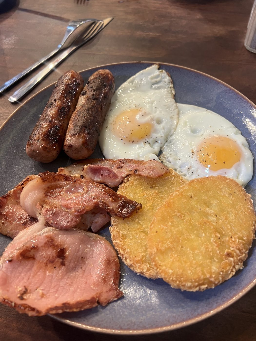 A cooked breakfast with sausages, bacon, fried eggs and a hash brown