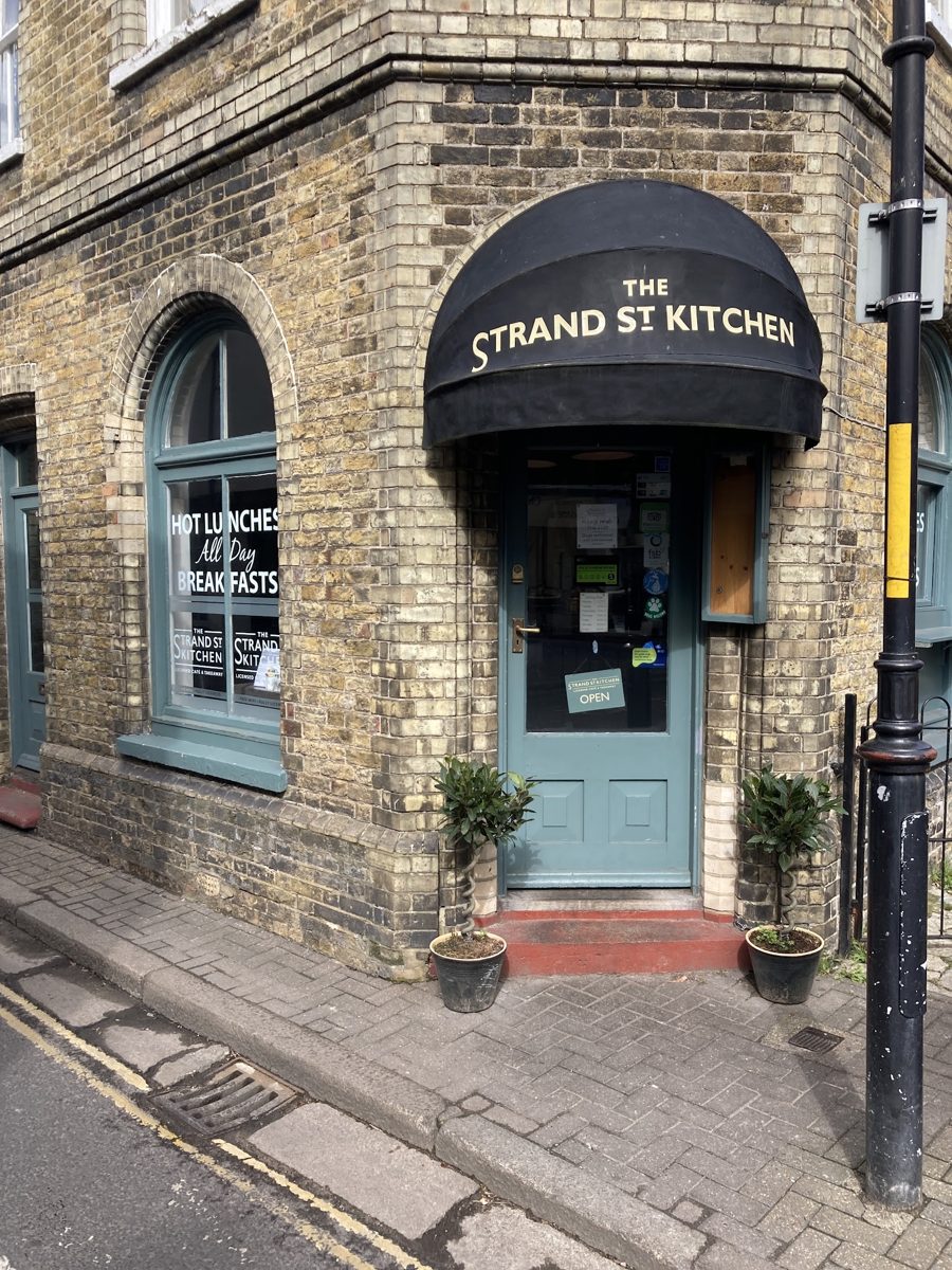 The brick corner building with a black STRAND ST KITCHEN awning over the door